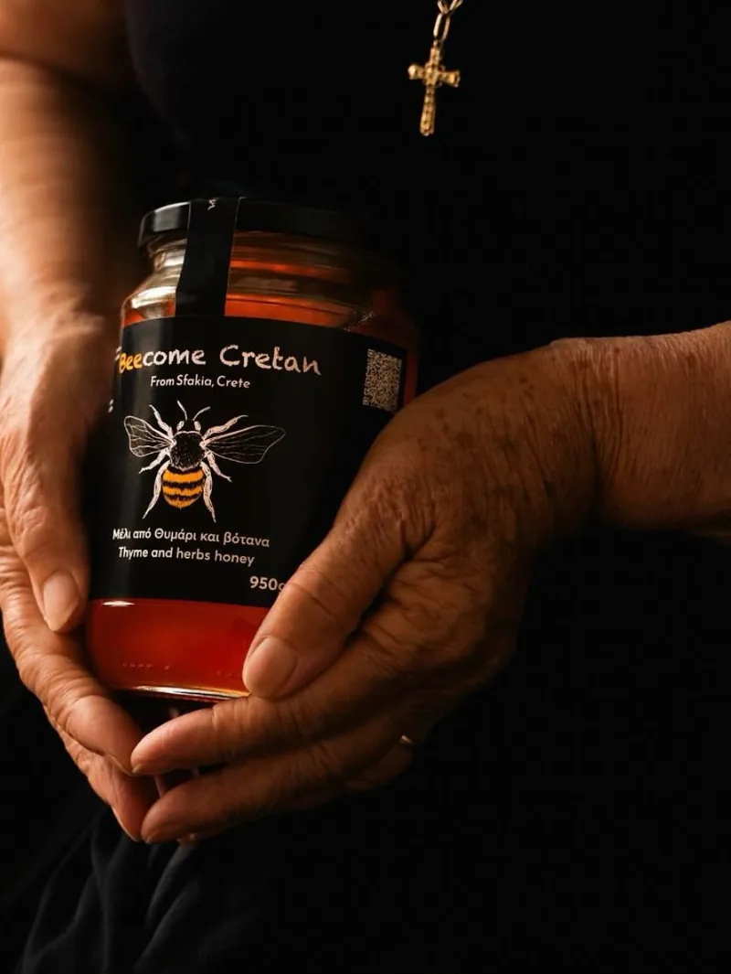 Χέρια κρατούν βάζο Beecome Cretan «Μέλι από θυμάρι και βότανα» 950gr με τη μαύρη ετικέτα